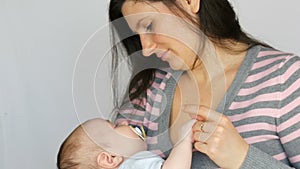 Young beautiful mother with long dark hair is holding a newborn infant baby of two months on white background in studio