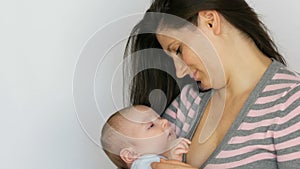 Young beautiful mother with long dark hair is holding a newborn infant baby of two months on white background in studio