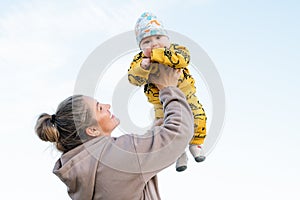 Young beautiful mother plays with her child outdoor. woman hugging her kid against the sea.