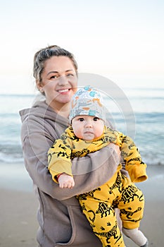 Young beautiful mother plays with her child outdoor. woman hugging her kid against the sea.