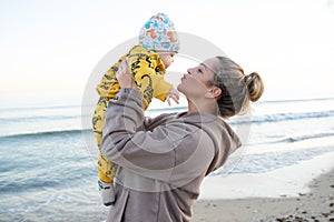 Young beautiful mother plays with her child outdoor. woman hugging her kid against the sea.