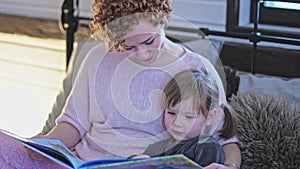 A young, beautiful mother reads a children`s book to her little daughter. Caring for a child. Preparation for sleep. Mom with her