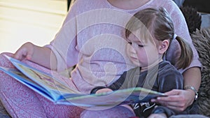 A young, beautiful mother reads a children`s book to her little daughter. Caring for a child. Preparation for sleep. Mom with her