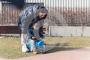 The young beautiful mother is taking care and teaching his small cute african child to ride a baby bike in a background