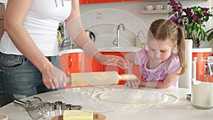 Young beautiful mother teaches daughter prepare dough in the kitchen