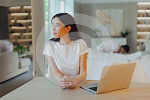 Young beautiful mother works on laptop while her husband looks after baby