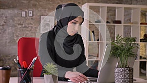 Young beautiful muslim girl in hijab is working with laptop in office, work concept, business concept, communication