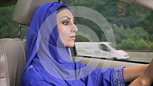 Young beautiful muslim woman in violet hijab driving car on the road