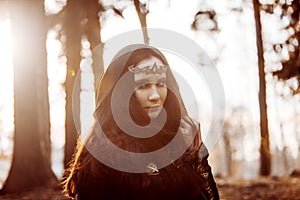 Young beautiful and mysterious woman in woods, in black cloak with hood, image of forest elf or witch