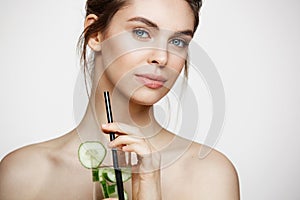 Young beautiful naked girl with perfect clean skin smiling looking at camera holding glass of water with cucumber slices