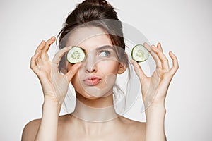 Young beautiful naked girl smiling hiding eye behind cucumber slice over white background. Beauty spa and cosmetology