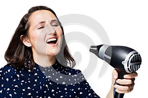 Beautiful brunette girl with eyes closed screaming singing into a Hairdryer on hand isolate the blue shirt happiness emotions the