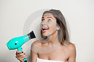 Young beautiful naked girl in towel singing with hairdryer.