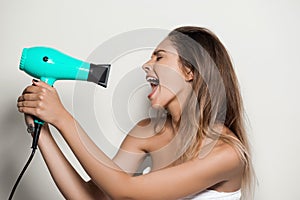 Young beautiful naked girl in towel singing with hairdryer.