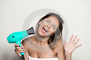 Young beautiful naked girl in towel singing with hairdryer.