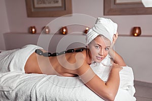 Young beautiful naked woman lying with black stones on her back in spa center