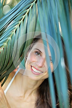 Young beautiful natural cheerful woman with healthy face and skin in exotic greenery. Closeup fresh face of attractive