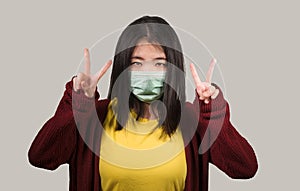 Young beautiful pacifist Asian Korean woman in face mask doing peace fingers symbol standing for human rights respect and freedom