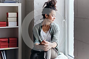 Young beautiful pensive woman with dark curly hair sitting on window sill in audience of university thoughtfully looking