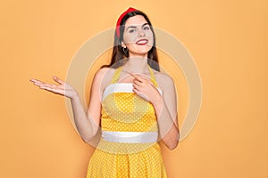 Young beautiful pin up woman wearing 50s fashion vintage dress over yellow background amazed and smiling to the camera while