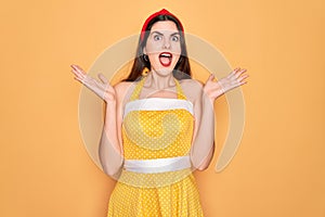 Young beautiful pin up woman wearing 50s fashion vintage dress over yellow background celebrating crazy and amazed for success