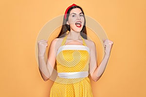Young beautiful pin up woman wearing 50s fashion vintage dress over yellow background celebrating surprised and amazed for success