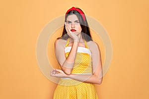 Young beautiful pin up woman wearing 50s fashion vintage dress over yellow background thinking looking tired and bored with