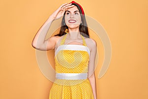 Young beautiful pin up woman wearing 50s fashion vintage dress over yellow background very happy and smiling looking far away with