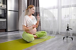 Young beautiful pleasant lady recording video online translation on mobile phone showing yoga exercises