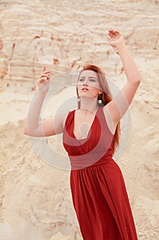 Young beautiful plus size Caucasian woman in red long dress posing in desert landscape with sand.
