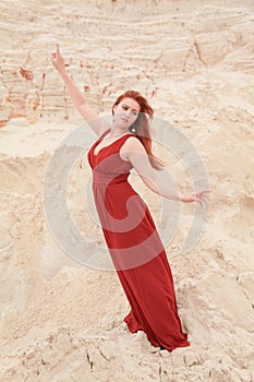 Young beautiful plus size Caucasian woman in red long dress posing in desert landscape with sand.