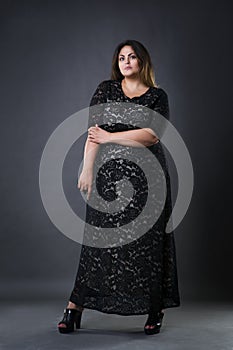 Young beautiful plus size model in black dres, xxl woman on gray studio background