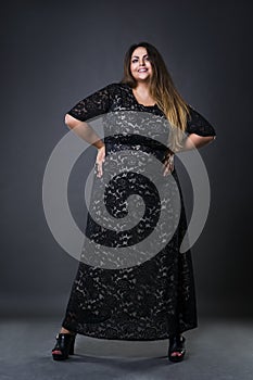 Young beautiful plus size model in black dres, xxl woman on gray studio background