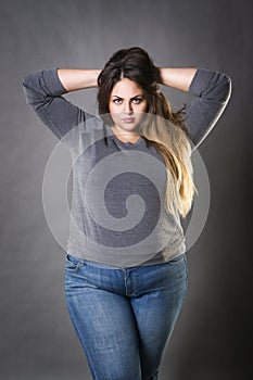 Young beautiful plus size model in blue jeans, xxl woman on gray background