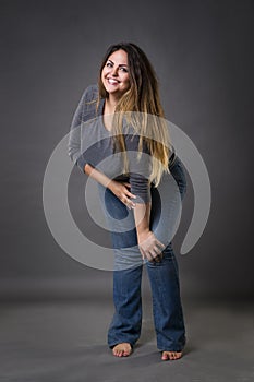 Young beautiful plus size model in blue jeans, xxl woman on gray studio background