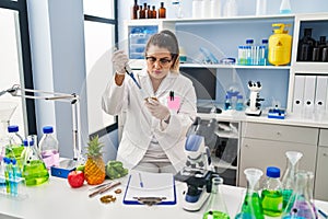 Young beautiful plus size woman scientist pouring liquid on green peas sample at pharmacy