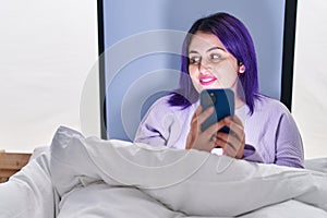 Young beautiful plus size woman using smartphone sitting on bed at bedroom