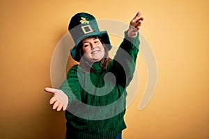 Young beautiful plus size woman wearing green hat with clover celebrating saint patricks day looking at the camera smiling with