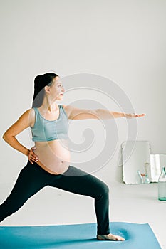 Young beautiful pregnant girl in sportswear doing yoga, doing asana Virabhadasana-Warrior Pose on the Mat in the Studio