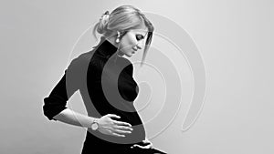 Young beautiful pregnant woman in black clothes hugs her tummy on a neutral background.