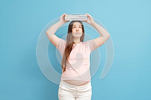 Young beautiful pregnant woman on a blue background with books on her head, pregnant student, expectant mother with books about