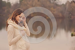 Young beautiful pregnant woman on cozy warm walk on autumn riverside, warm toned, soft focus