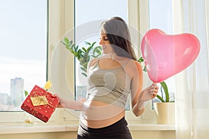 Young beautiful pregnant woman with gift box and balloon heart