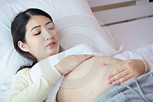 Young beautiful pregnant woman lie down and touching belly on bed at home. Pregnancy, motherhood, love and expectation concept