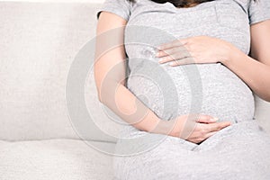 Young beautiful pregnant woman sitting on gray sofa at home and