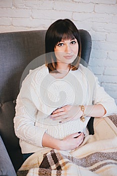 Young beautiful pregnant woman sitting on a grey chair