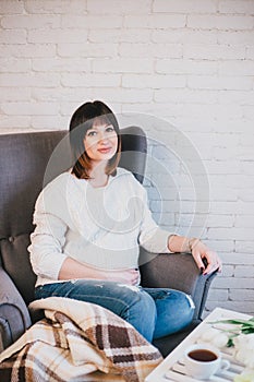 Young beautiful pregnant woman sitting on a grey chair