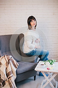 Young beautiful pregnant woman sitting on a grey chair