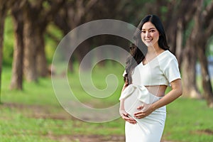 Young beautiful pregnant woman stroking her belly in park