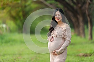 Young beautiful pregnant woman stroking her belly in park